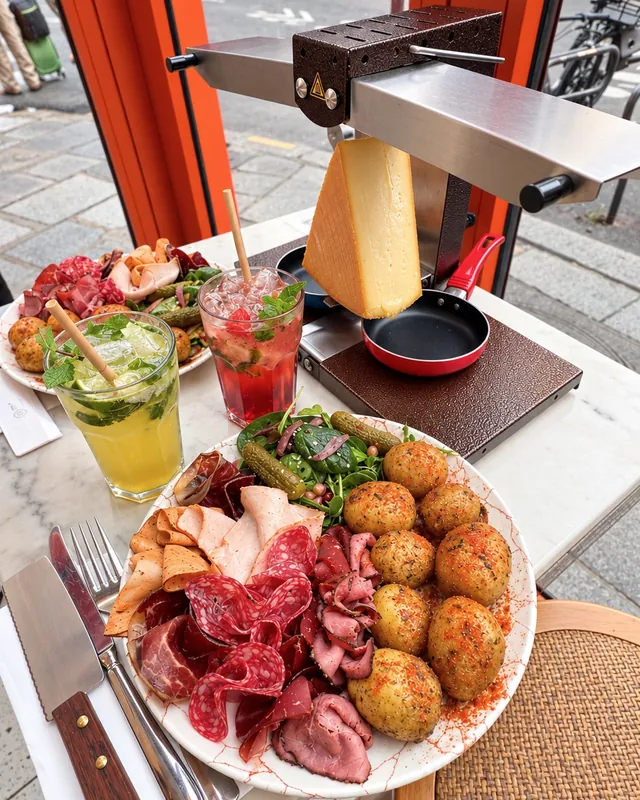 La raclette à volonté chez Oma : l'appareil sur la table, le fromage qui fond, une assiette de charcuterie et de pommes de terre rôties, rue Beaurepaire à Paris 10